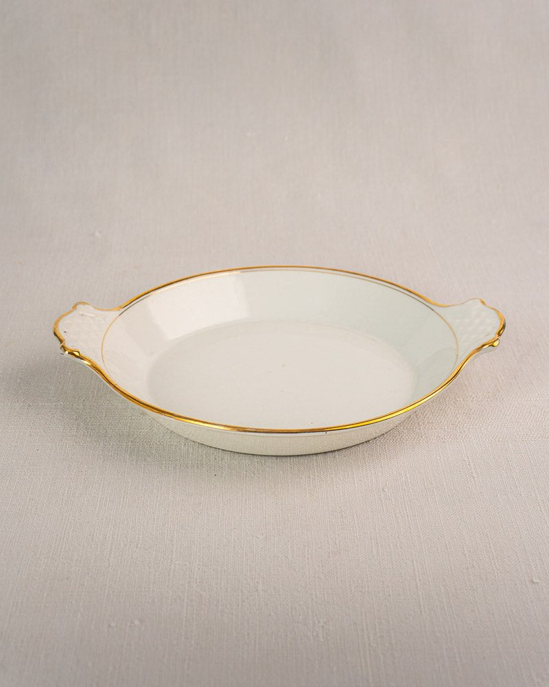 Shallow white ceramic French serving dish with gold rim and handles, 19th-century Vieux Paris porcelain, on gray surface.