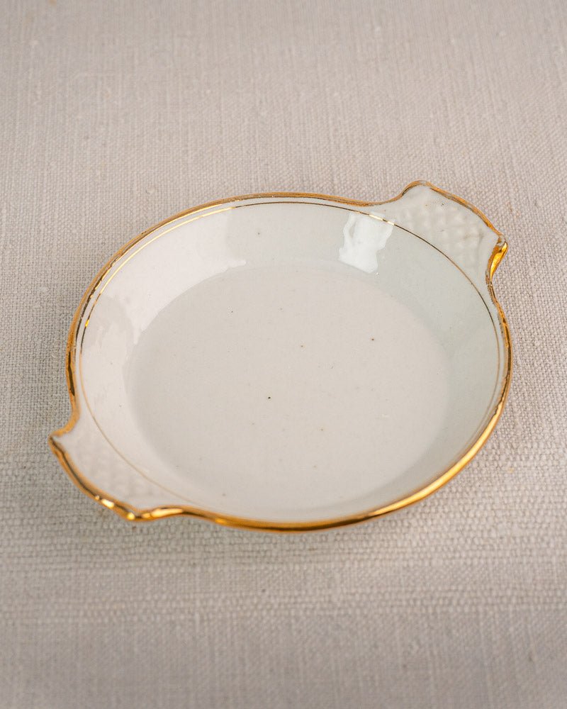 Antique French Vieux Paris porcelain serving dish with gold trim and handles on beige fabric.