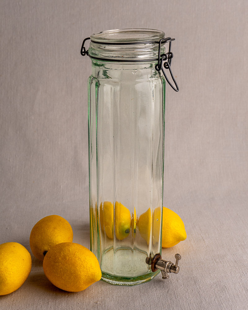 Antique French glass vinaigrier with metal lid, latch, and spigot on a light surface.