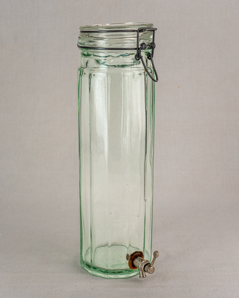 Antique French glass vinaigrier with metal lid, latch, and spigot on a light surface.