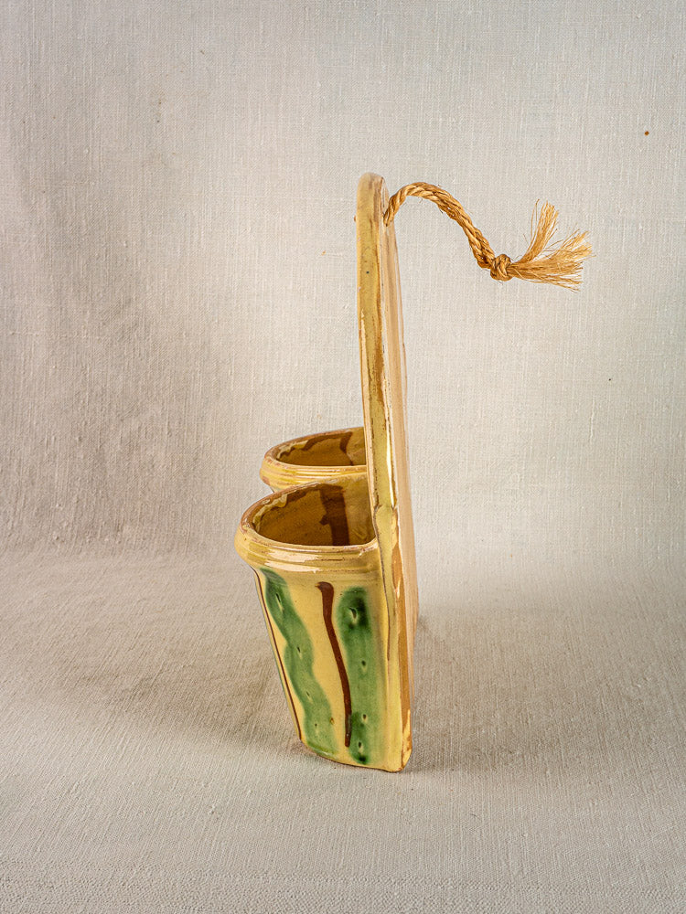 Vintage French glazed earthenware wall pocket cutlery holder with green and brown finish, on woven fabric.