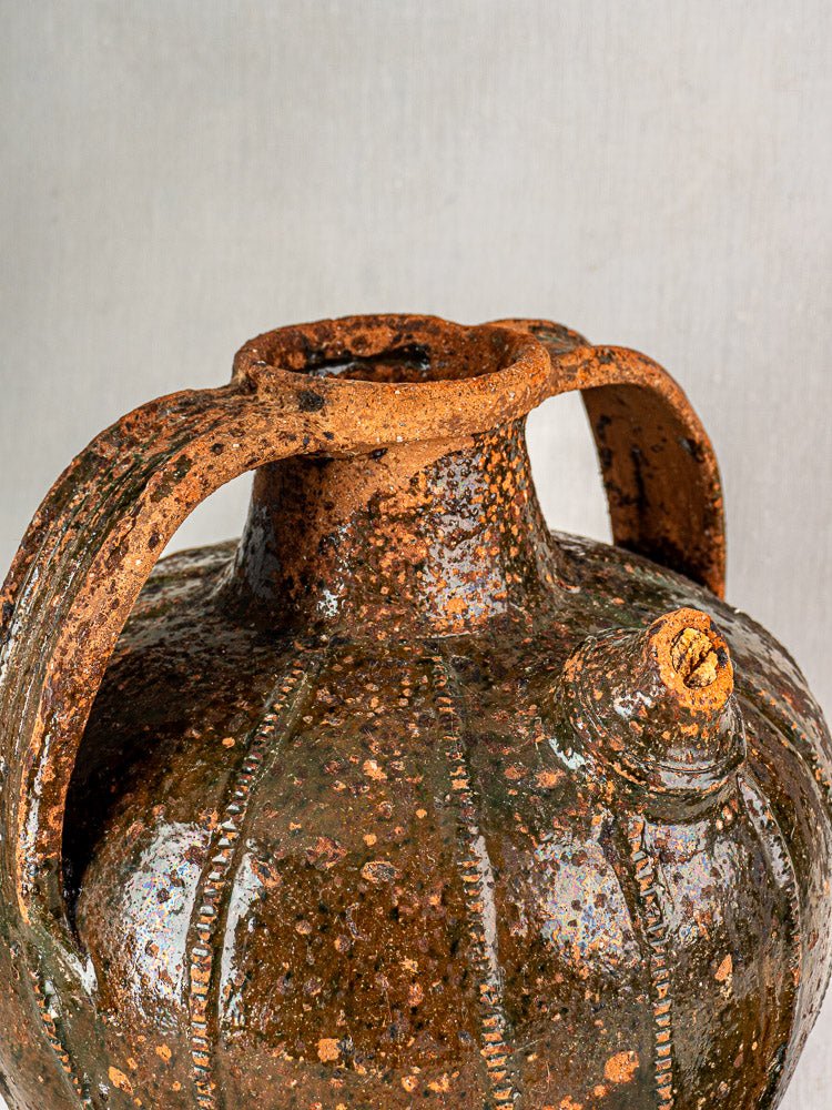 Antique French terracotta oil cruche with rustic texture, dual handles, and brown-green speckled glaze.