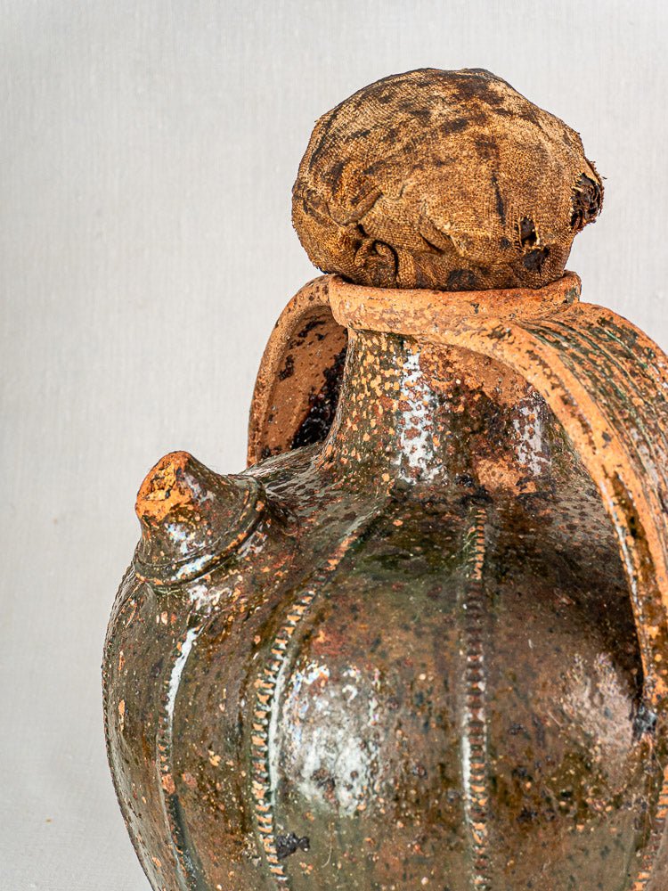 Antique French glazed terracotta oil cruche with spout, curved handle, and mottled brown-green finish.