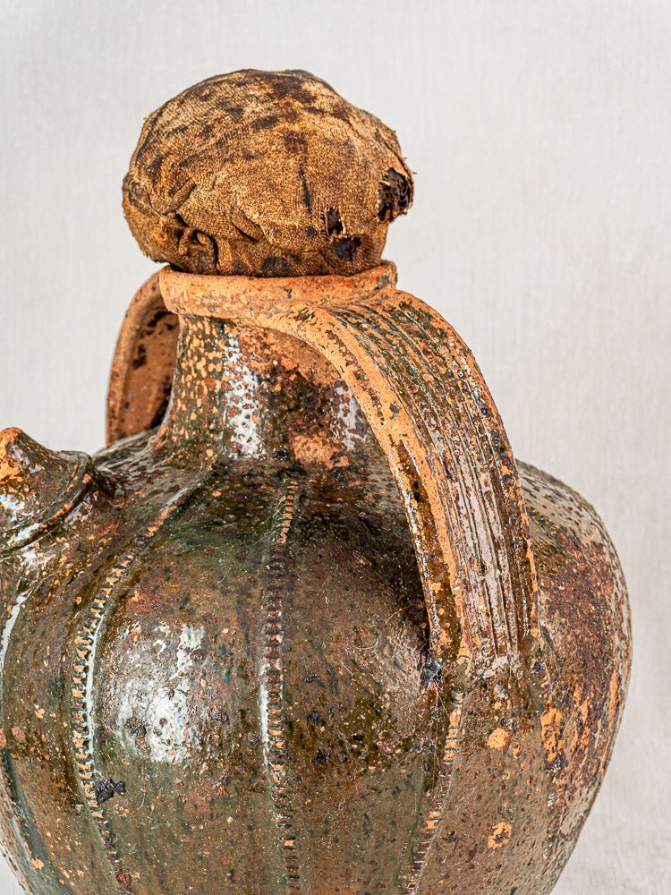 Antique French glazed terracotta cruche with ribbed surface, fabric-wrapped stopper, and aged patina.