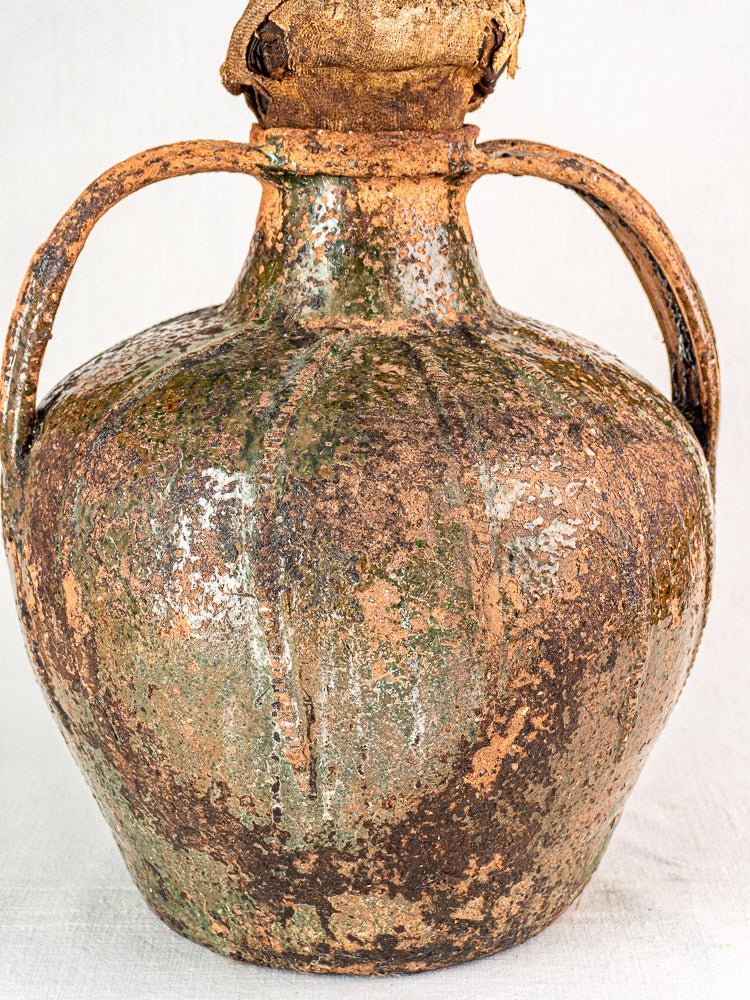 Antique French terracotta cruche with two curved handles, mottled brown-green glaze, and cloth stopper.