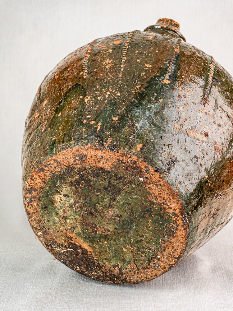 Antique French walnut oil cruche with mottled green and brown glazed terracotta surface on neutral background.