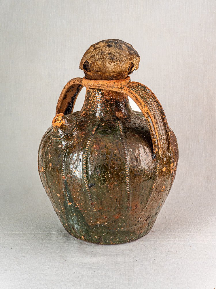 Antique French terracotta oil cruche with dark green glaze, curved handles, cork top, neutral background.