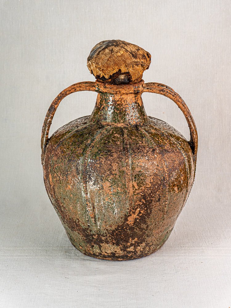 Antique French walnut oil cruche in glazed terracotta with dual handles, rustic brownish-green finish, plain backdrop.