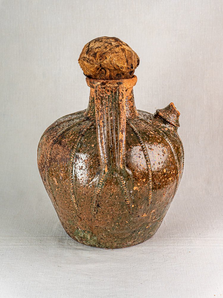 Antique French terracotta oil cruche with rustic brown glaze, wide body, and narrow neck on neutral backdrop.