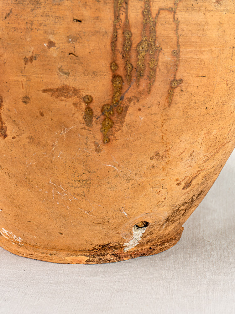 Antique French walnut oil jar in weathered Auvergne terracotta with original cork, light gray surface.