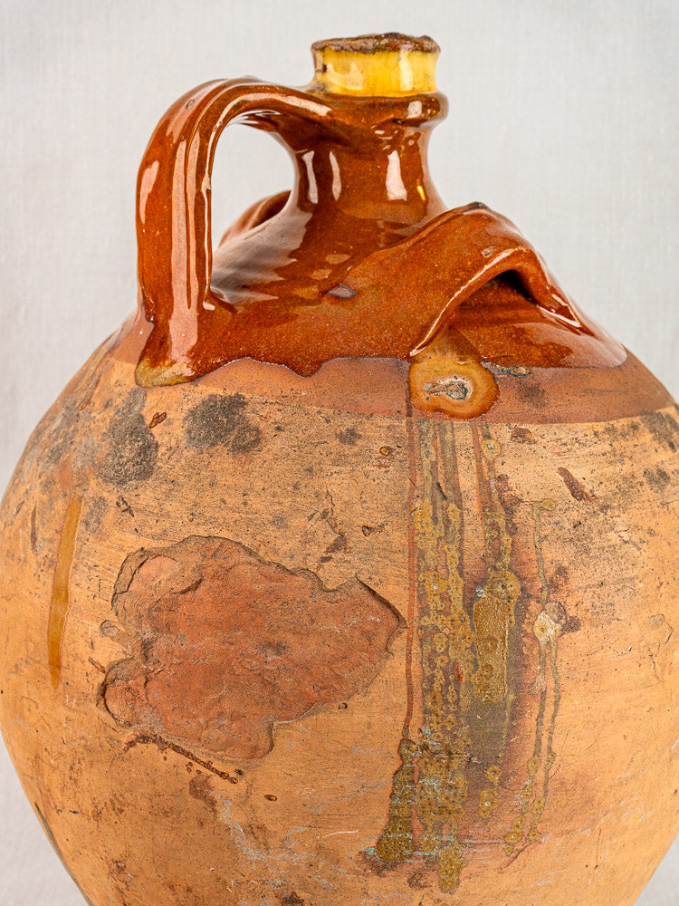 Antique French terracotta walnut oil jar with original cork, weathered glazing, and glossy brown handle.