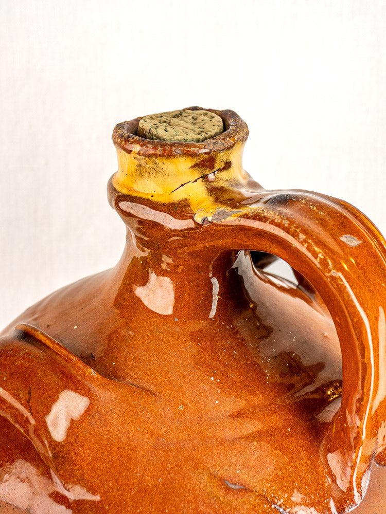 Antique French terracotta walnut oil jar from Auvergne with cork stopper and curved handle on white background.