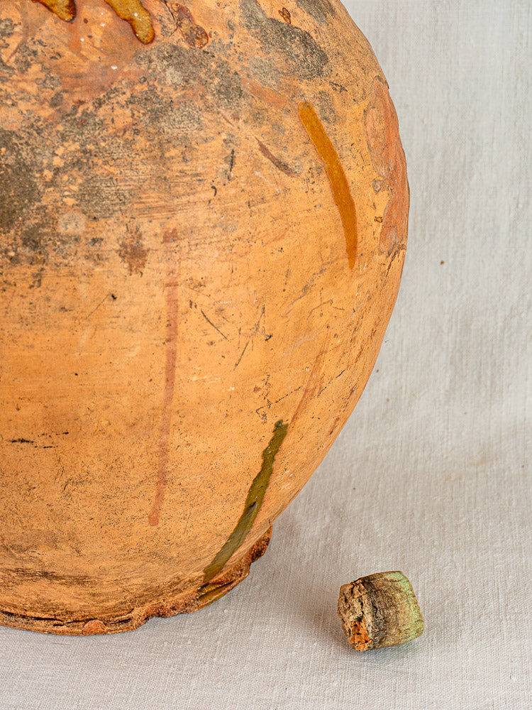 Antique French terracotta oil jar with original cork and rustic patina on light fabric.