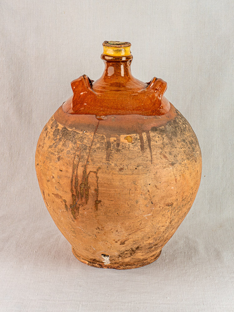 Vintage French brown clay jug with narrow neck and two handles, original cork, plain background.