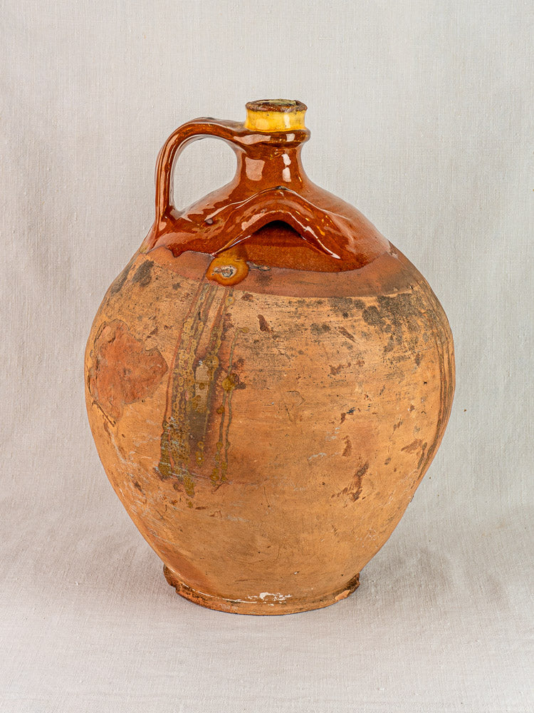 Antique French Auvergne terracotta jug with brown-glazed top, original cork, on light fabric.