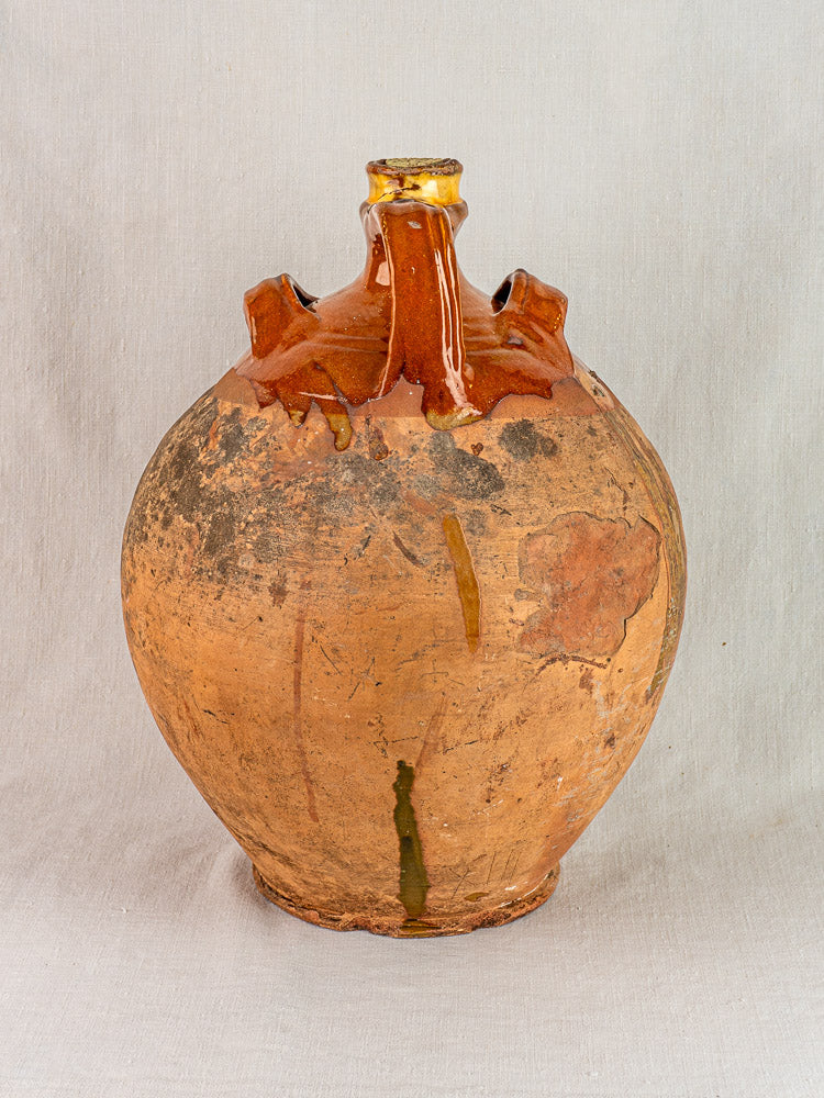 Antique French Auvergne terracotta oil jar with narrow neck, side handles, and original cork on gray fabric.