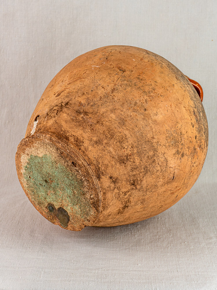 Antique French walnut oil jar in Auvergne terracotta with original cork, weathered patina, on fabric.