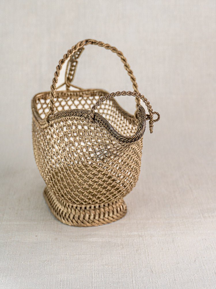 Antique French Belle Epoque silver plate wine bottle holder with twisted handles on neutral fabric background.