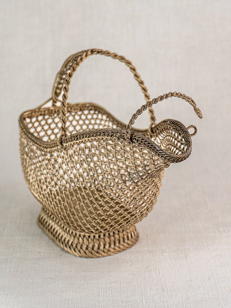Antique French silver plate wirework wine bottle holder with elegant twisted handles on light fabric background.