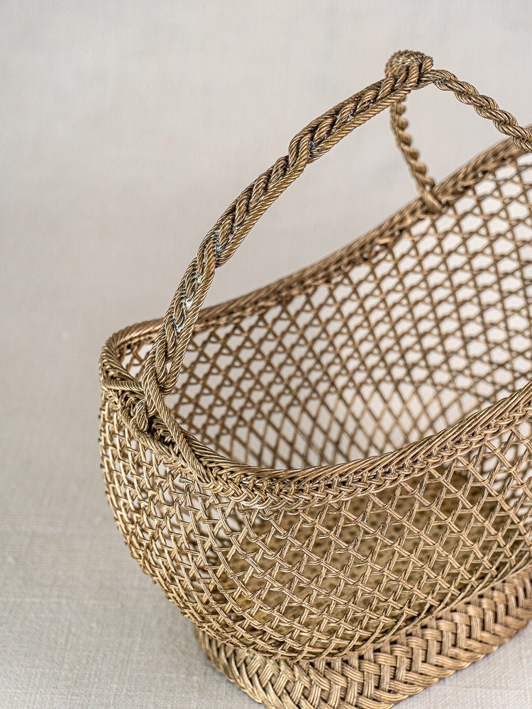 Antique French wine bottle holder with Belle Epoque silver plate wirework and braided handle on a light textured surface.