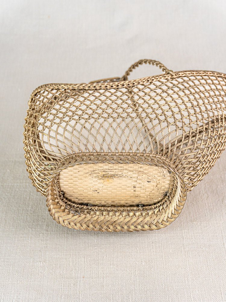 Antique French Belle Epoque oval silver plate wine bottle holder with open lattice wirework on light fabric.