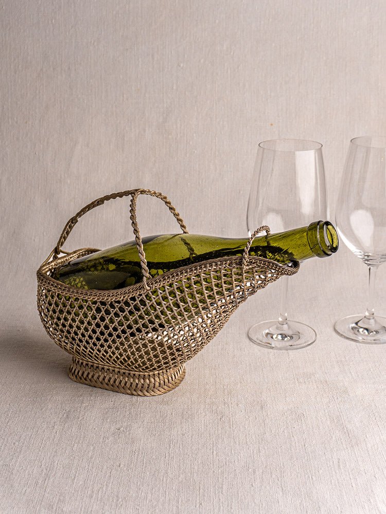 Antique French silver plate wirework wine bottle holder with green bottle and two empty glasses.