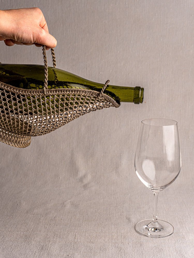 Antique French Belle Epoque silver plate wine bottle holder with green bottle above empty glass.