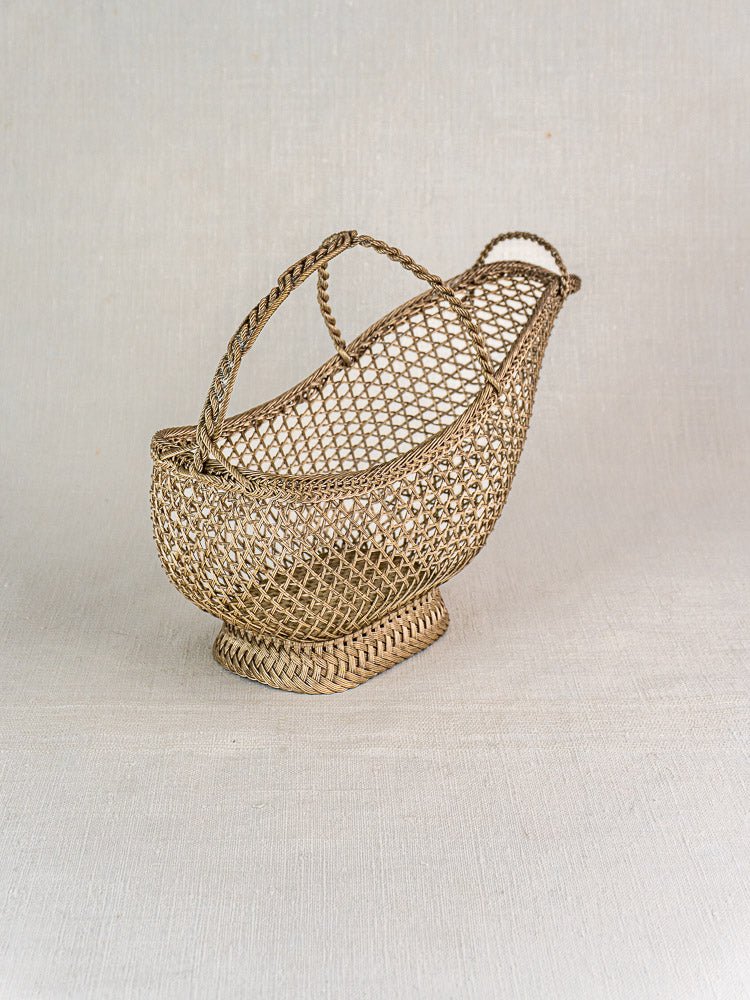 Antique French silver plate wine bottle holder with Belle Époque wirework on neutral fabric background.