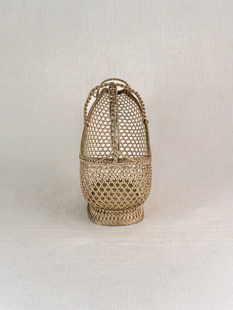 Antique French Belle Époque silver plate wine bottle holder with braided handle on neutral fabric.