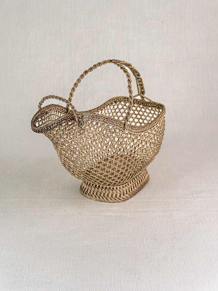 Antique French silver plate wine bottle holder with ornate base and curved handle on textured surface.