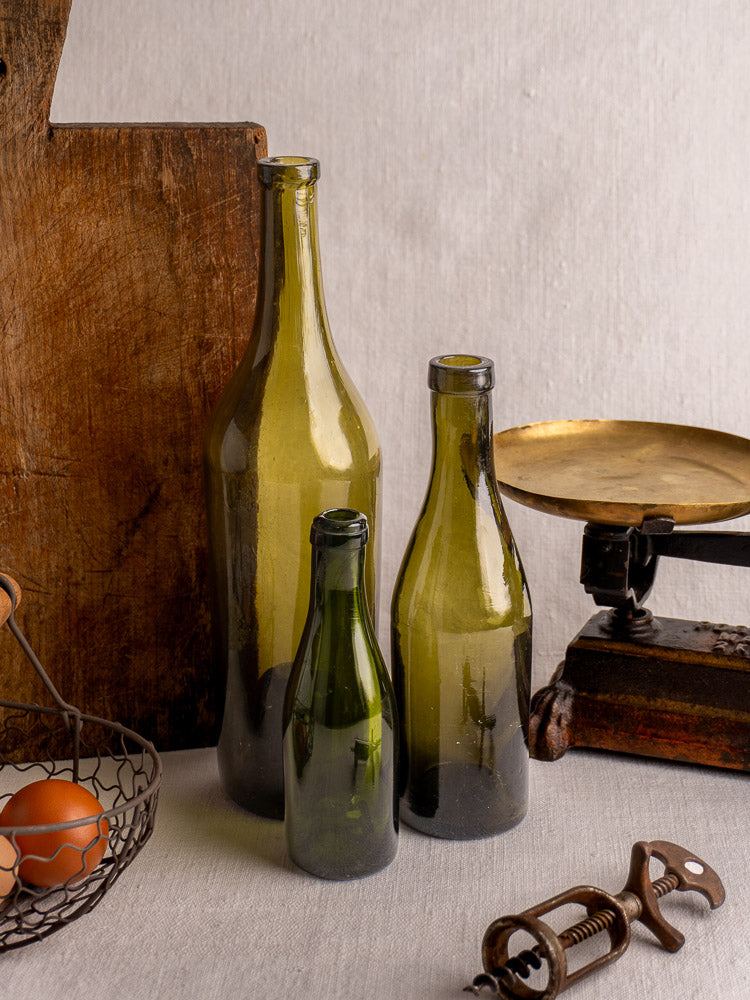 Set of three mid-19th century antique French hand blown wine bottles on table with vintage accessories.