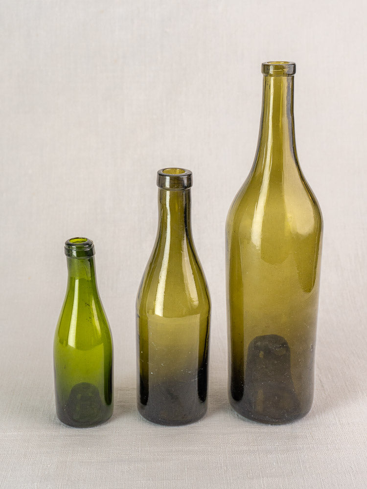 Set of three mid-19th century French hand blown wine bottles in olive green glass, arranged by height.