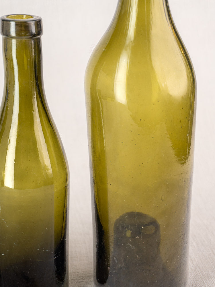 Set of three mid 19th-century antique French hand-blown wine bottles on light surface.