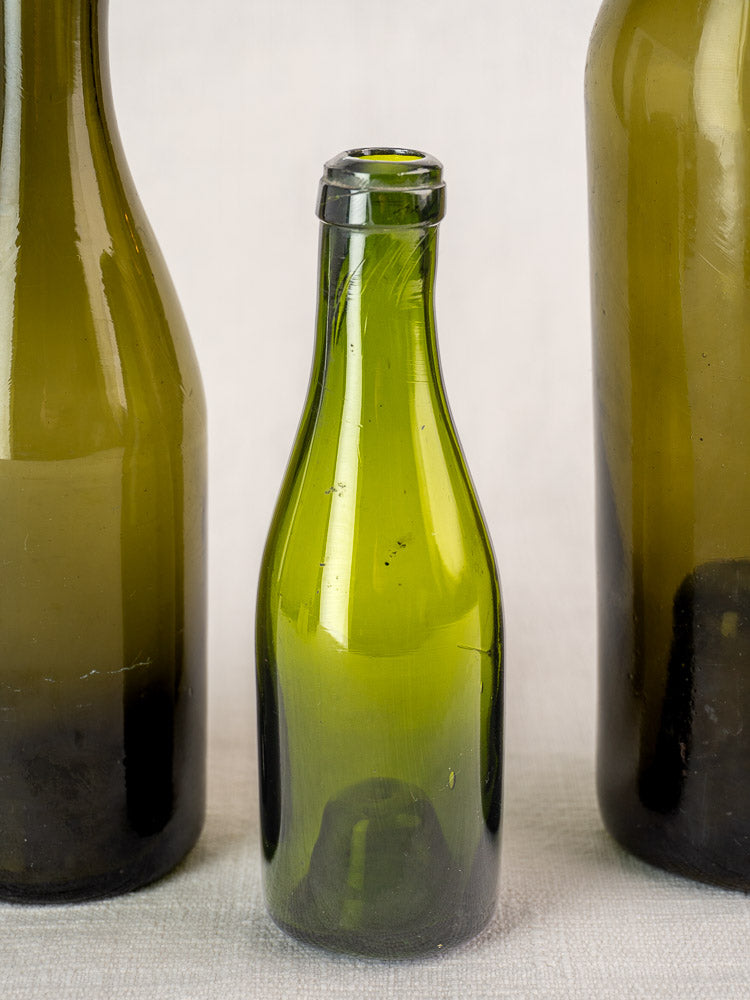 Set of three antique French hand blown wine bottles, mid 19th century, on a light surface.