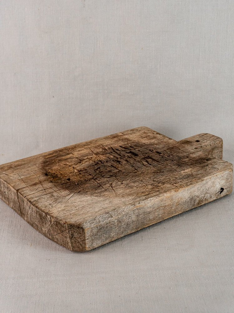 Antique French solid wood bread board with knife marks and rustic rectangular design on gray surface.