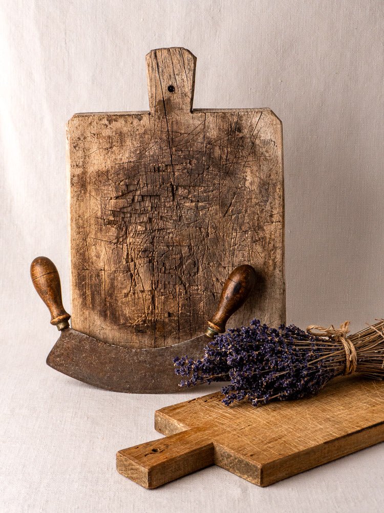 Antique French solid wood bread board with curved double-handled blade, smaller board, and dried lavender.