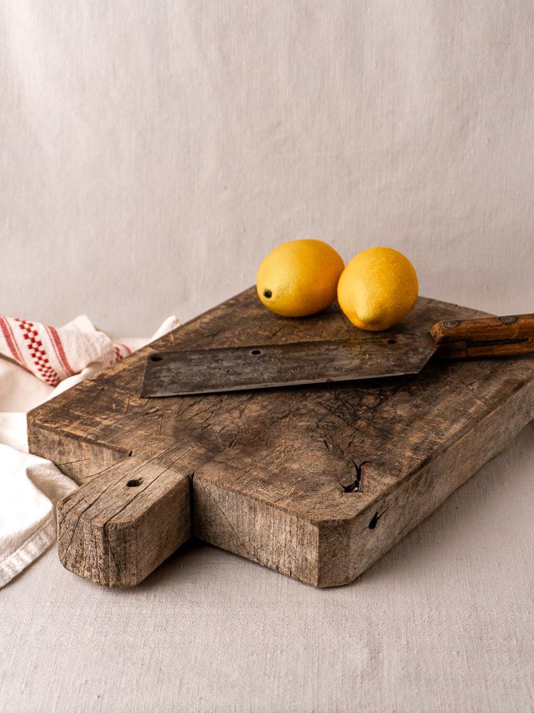 Late 19th century French antique wood bread board with knife and two lemons, on neutral fabric.