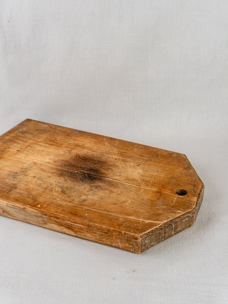 Antique 19th century French cutting board with dark stain and a corner hole on gray fabric.