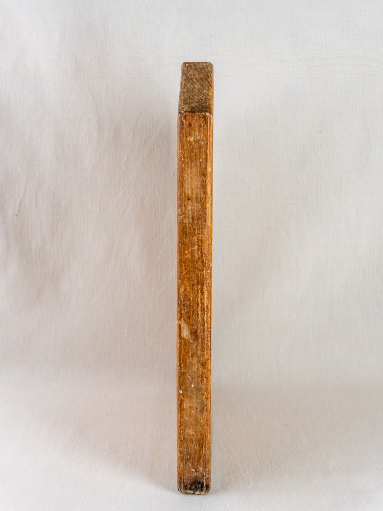Antique 19th-century French cutting board, weathered rectangular wood, upright on neutral textured surface.