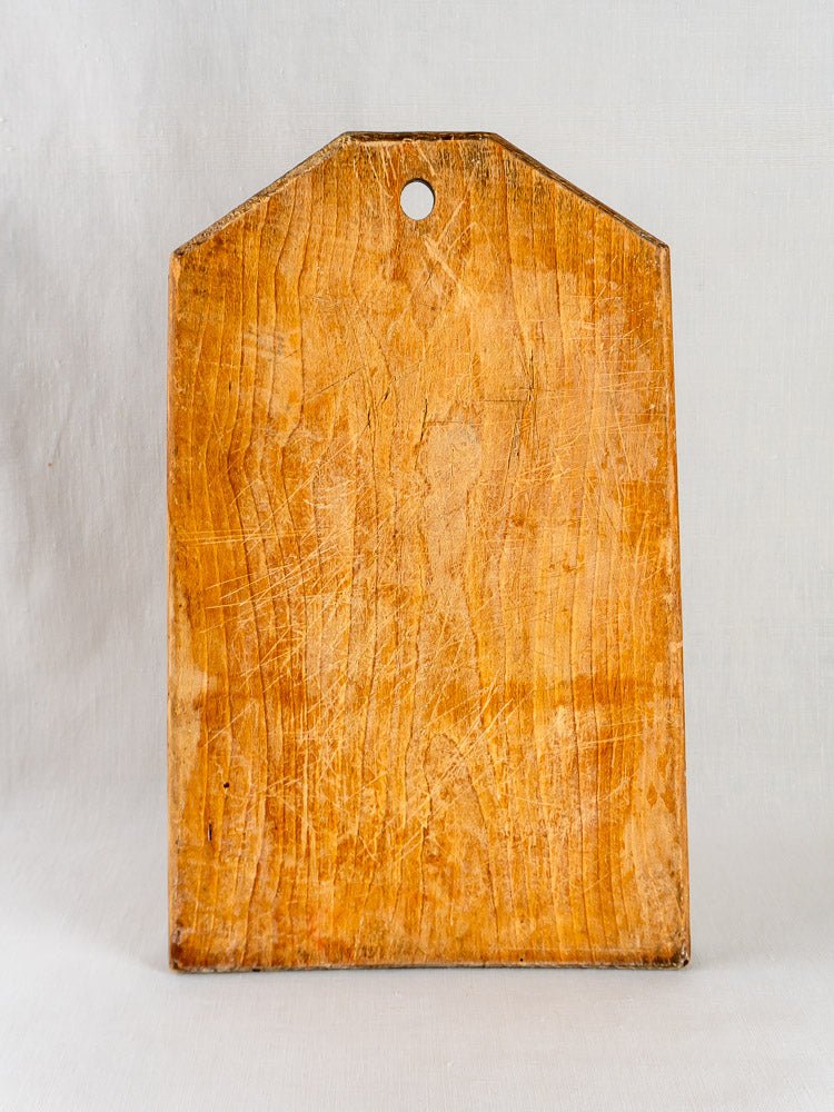 Antique French 19th-century tombstone cutting board with pointed top and central hole, showing knife marks.