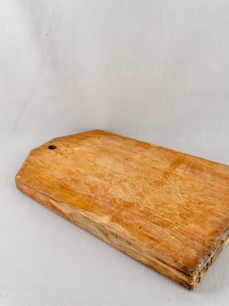 Antique 19th-century French tombstone cutting board with corner hole, on light fabric surface.