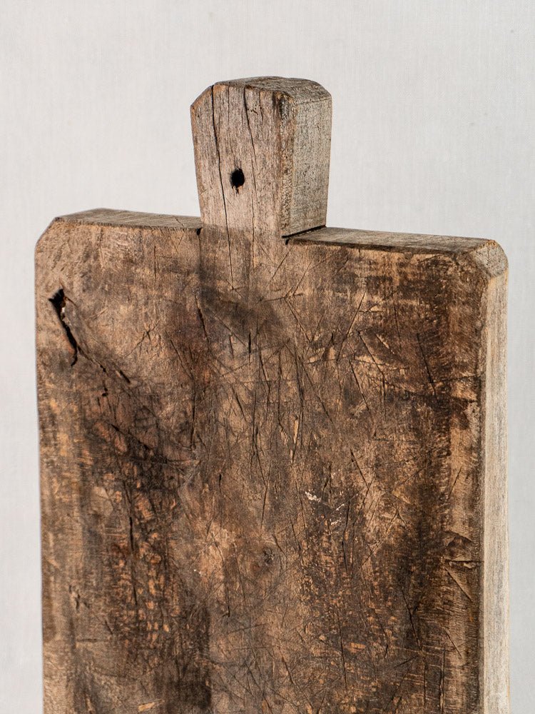 Antique French bread board, late 19th-century solid wood, worn handle, aged scratches, light background.