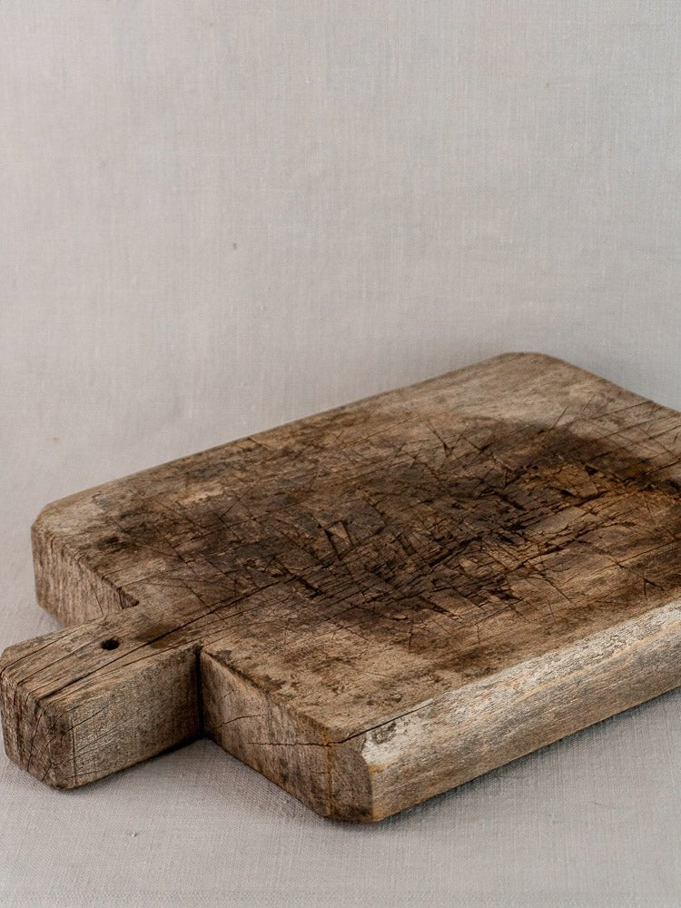 Antique French bread board in solid wood with deep knife marks and dark patina on gray fabric.