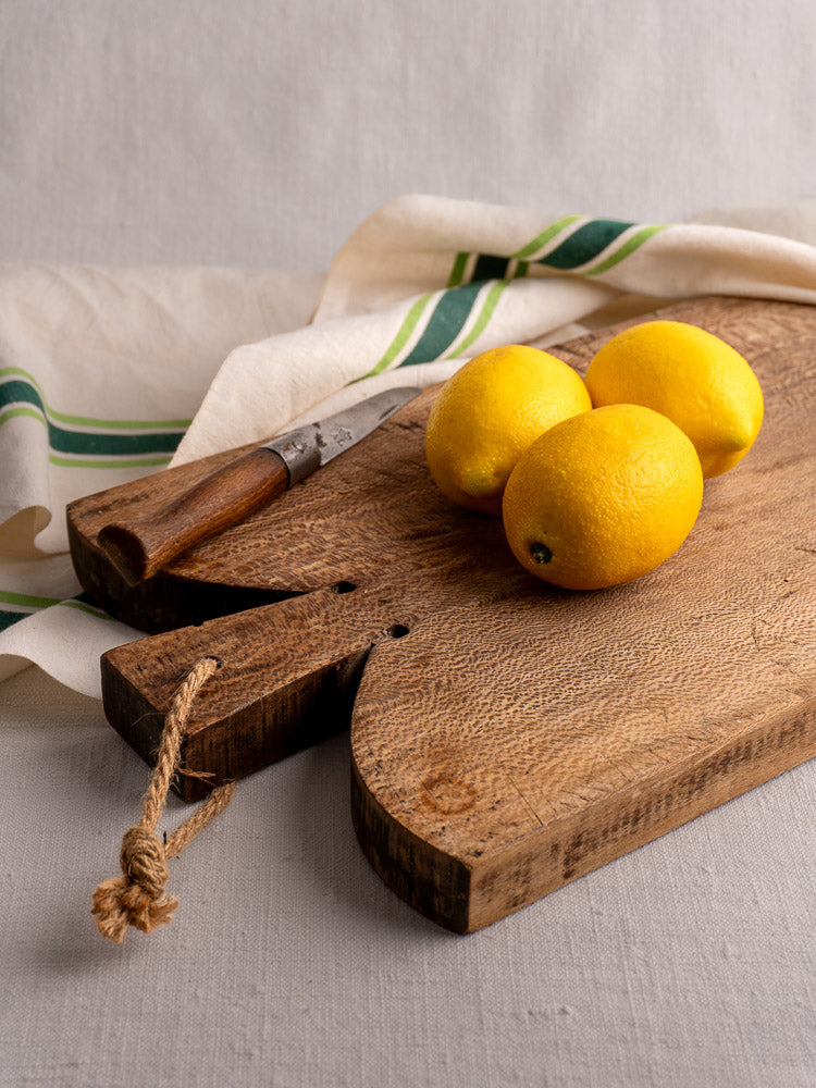 Antique French cutting board with patina, rectangular shape, notched top, and rope loop handle on a light gray background.
