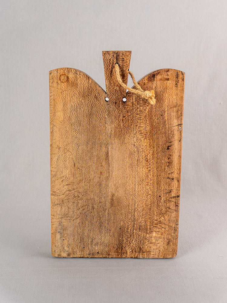 Antique French cutting board with patina, rectangular shape, notched top, and rope loop handle on a light gray background.