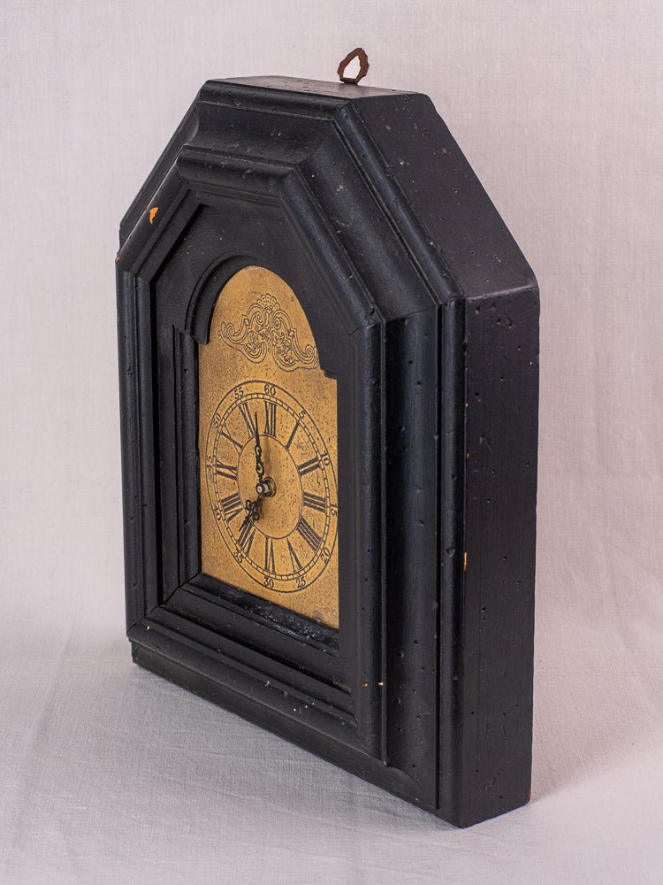 Antique French wall clock, late 19th century, black painted wood frame, gold face at 8:00, light fabric backdrop.