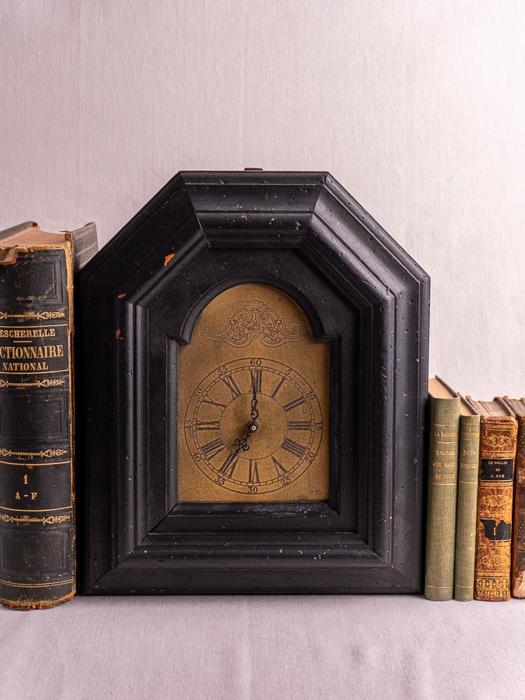 Antique French black painted wood wall clock, late 19th century, displayed beside worn vintage books.