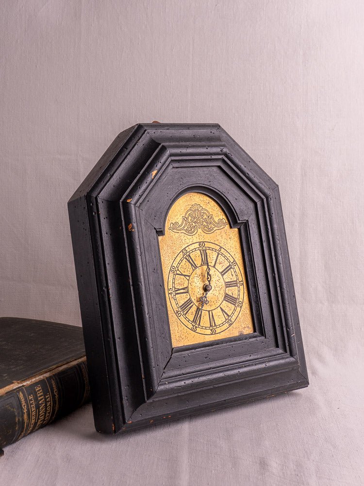 Antique French black wood wall clock, late 19th century, displayed beside a vintage book.