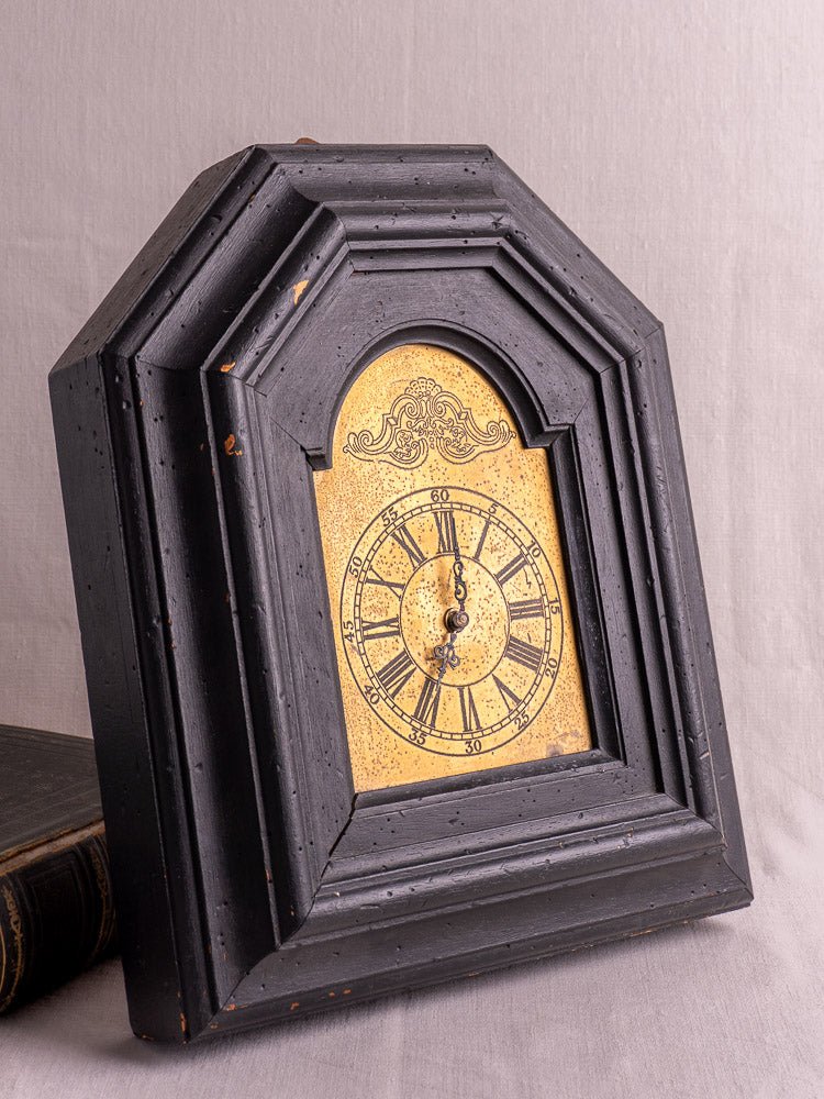 Antique French wall clock with distressed black wood frame and ornate gold Roman numeral face.