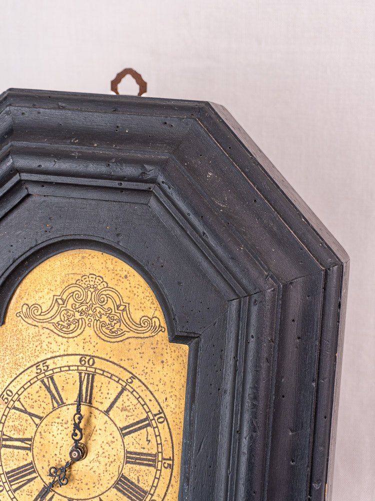 Antique French wall clock top right corner in black wood, yellow face with Roman numerals.